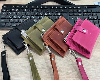 May include: Four leather wallets with zipper closures and wrist straps. The wallets are in black, green, brown, and pink.