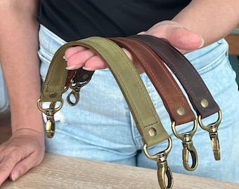 Può includere: Tre tracolle in pelle per borsa nei colori verde oliva, marrone rossiccio e marrone scuro. Ogni tracolla presenta bordi cuciti, rivetti in metallo color ottone anticato e moschettoni girevoli abbinati su entrambe le estremità.