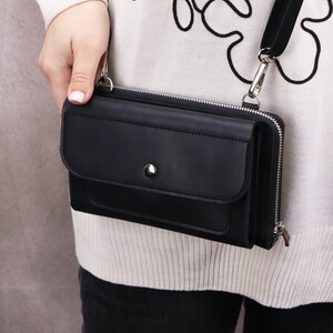 May include: A black rectangular crossbody bag featuring a front flap with a silver-toned snap button closure, a main zippered compartment, and a detachable black shoulder strap with silver metal hardware clips attached to the sides of the bag.