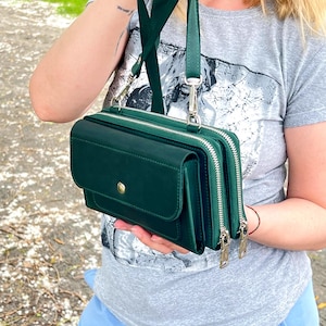Op de afbeelding: Een donkergroene rechthoekige schoudertas met een voorflap voorzien van een goudkleurige drukknoopsluiting, twee hoofdvakken met ritssluiting en een bijpassende verstelbare schouderriem bevestigd met zilverkleurige metalen clips.