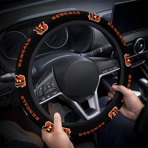 Könnte beinhalten: Schwarze Lenkradabdeckung mit orangenen Bengals-Logos und -Text. Die Abdeckung ist an einem Autolenkrad angebracht.