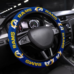 Pode incluir: Uma capa de volante azul e amarela com o logotipo dos Los Angeles Rams e a palavra "Rams" repetida ao redor da capa.