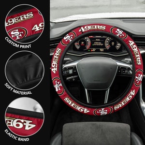 May include: Red and gold steering wheel cover with the San Francisco 49ers logo and the words "49ers" repeated around the cover. The cover is made of soft material and has an elastic band.