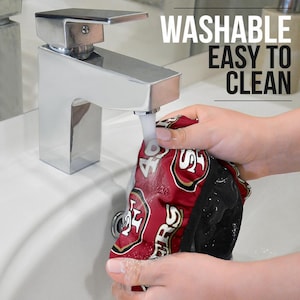 May include: A red and black fabric shower cap with the San Francisco 49ers logo and the text "49ers" is being rinsed under a faucet. The text "WASHABLE EASY TO CLEAN" is visible in the upper right corner of the image.