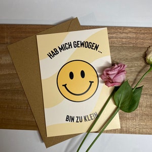 Könnte beinhalten: Eine gelbe Karte mit einem schwarzen Smiley und dem Text "HAB MICH GEWOGEN... BIN ZU KLEIN" in Schwarz.