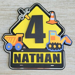 Puede incluir: Se&ntilde;al de construcci&oacute;n amarilla con un n&uacute;mero 4 negro, una llave inglesa, un cono de tr&aacute;fico y un veh&iacute;culo de construcci&oacute;n amarillo. La se&ntilde;al tiene una pancarta negra en la parte inferior con el nombre "NATHAN" en letras blancas.