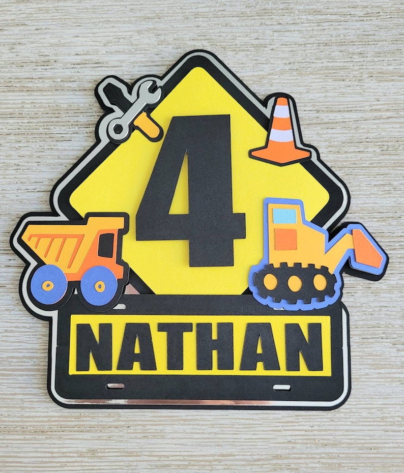 Puede incluir: Se&ntilde;al de construcci&oacute;n amarilla con un n&uacute;mero 4 negro, una llave inglesa, un cono de tr&aacute;fico y un veh&iacute;culo de construcci&oacute;n amarillo. La se&ntilde;al tiene una pancarta negra en la parte inferior con el nombre "NATHAN" en letras blancas.