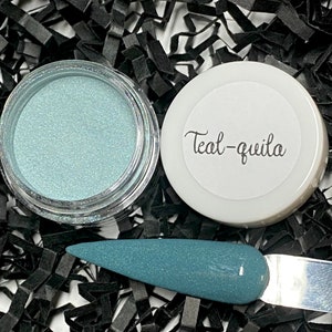 May include: A jar of teal-colored powder next to a white-lidded container with the text "Teal-quila." A nail swatch displays the same teal color. The background is black.
