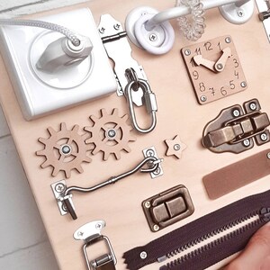 May include: A wooden activity board with various textures and activities for children. It features a clock, gears, a zipper, a latch, a hook and eye, a hasp, and a toggle latch.