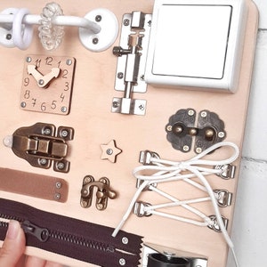 May include: A wooden busy board with various activities for children, including a clock, a zipper, a latch, a star, a toggle, a buckle, a shoelace, and a light switch.