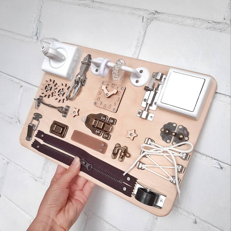 May include: A wooden activity board with various textures and activities for children. It features a zipper, a clock, a latch, a toggle switch, a buckle, a knob, a  lace, a  gear, a  star, and a  plug.