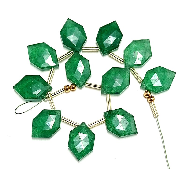 May include: A strand of green gemstone beads with faceted surfaces. The beads are strung on a wire with gold-colored spacers.
