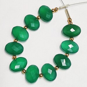 Puede incluir: Una hebra de cuentas de piedras preciosas verdes con separadores dorados. Las cuentas son de forma ovalada y tienen un acabado facetado.