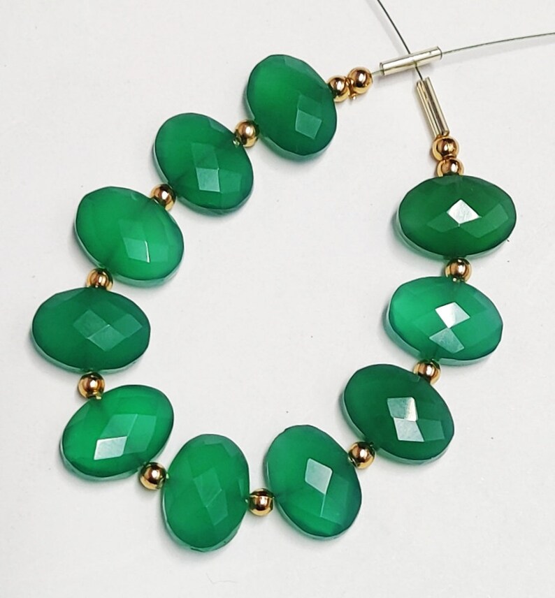 Puede incluir: Una hebra de cuentas de piedras preciosas verdes con separadores dorados. Las cuentas son de forma ovalada y tienen un acabado facetado.