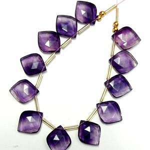 May include: A strand of purple amethyst gemstone beads with gold spacers. The beads are faceted and have a teardrop shape.