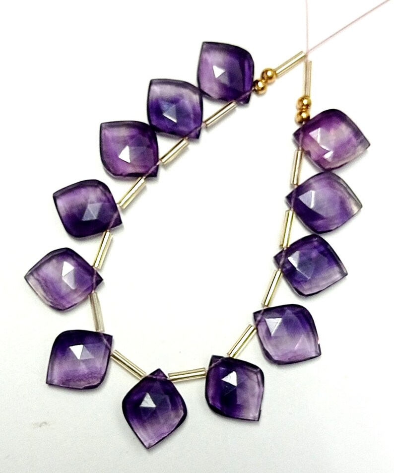 May include: A strand of purple amethyst gemstone beads with gold spacers. The beads are faceted and have a teardrop shape.