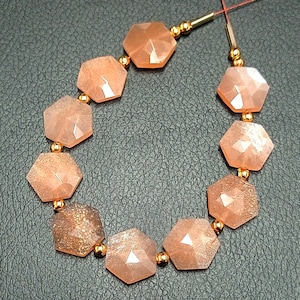 May include: A strand of orange sunstone beads with gold spacers. The beads are faceted and have a hexagonal shape.