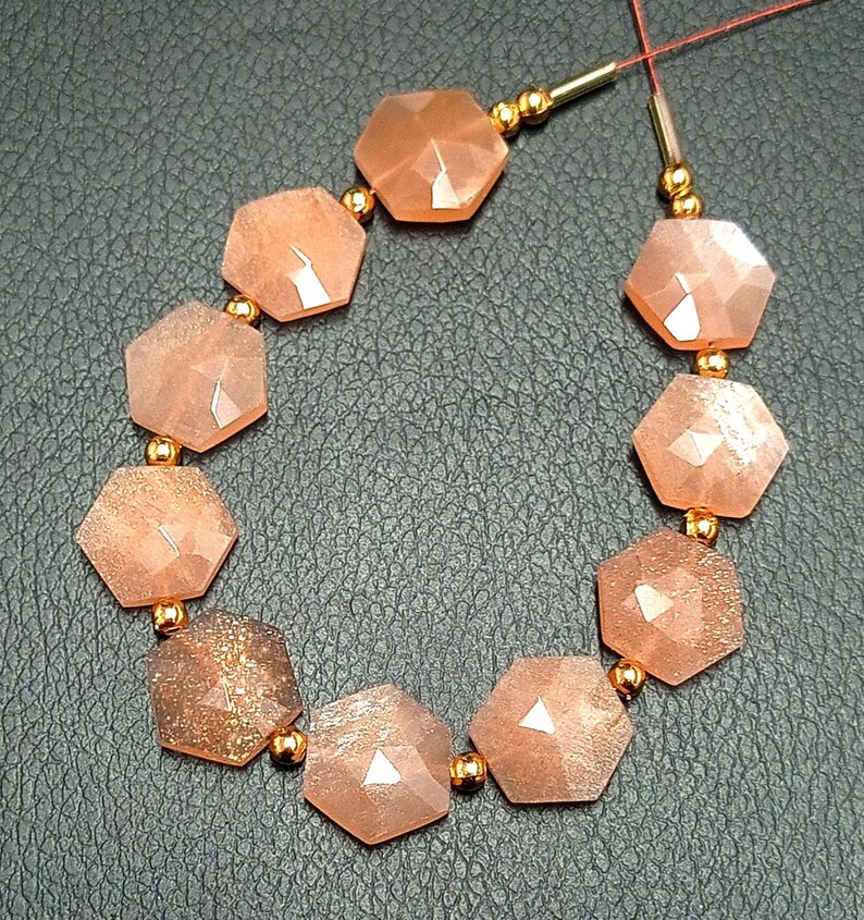 May include: A strand of orange sunstone beads with gold spacers. The beads are faceted and have a hexagonal shape.
