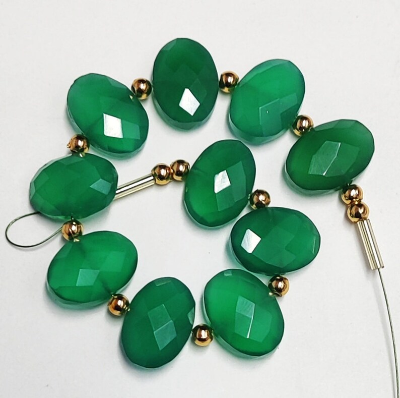 Puede incluir: Una hebra de cuentas de piedras preciosas verdes con separadores dorados. Las cuentas son de forma ovalada y tienen un acabado facetado.