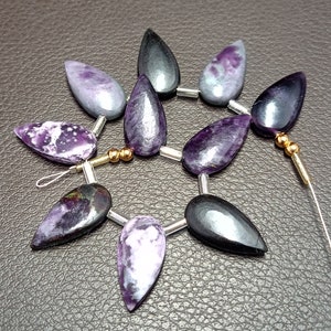 May include: A strand of purple and black gemstone beads, each bead is shaped like a teardrop. The beads are strung on a silver wire with gold spacers.