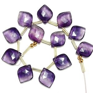 May include: A strand of purple amethyst gemstone beads with gold spacers. The beads are faceted and have a square shape with rounded corners.