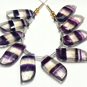 May include: A strand of 10 faceted, purple and white striped fluorite gemstone beads. The beads are all different sizes and shapes, but they are all strung together on a silver wire.