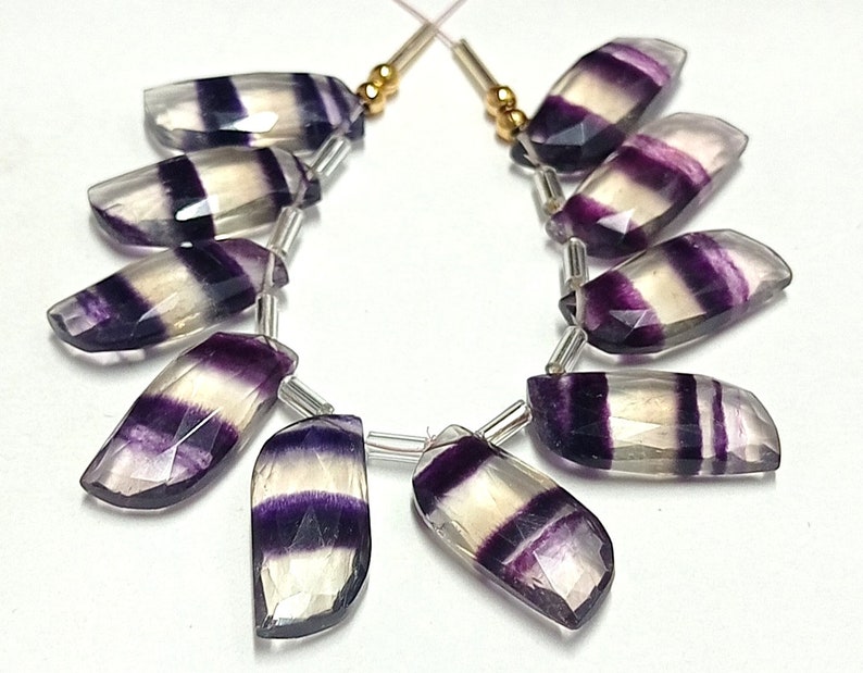 May include: A strand of 10 faceted, purple and white striped fluorite gemstone beads. The beads are all different sizes and shapes, but they are all strung together on a silver wire.