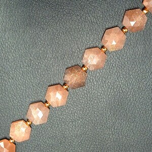 May include: A strand of faceted sunstone beads with a gold-toned metal spacer between each bead. The beads are a light peach color with a shimmery, iridescent finish.