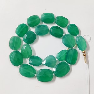 Peut inclure: Un collier de perles de pierres précieuses vertes, chaque perle est facetée et de forme ovale. Les perles sont enfilées sur un cordon blanc avec un fermoir doré.