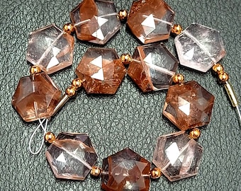 May include: A strand of faceted, hexagonal, clear quartz beads with a brown, reddish hue. The beads are strung on a wire with gold-colored spacers.