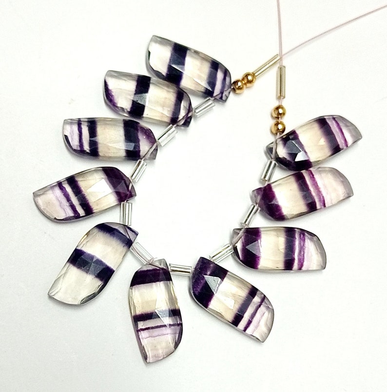 May include: A strand of 10 faceted fluorite beads with white and purple stripes. The beads are strung on a silver wire with gold beads and spacers.