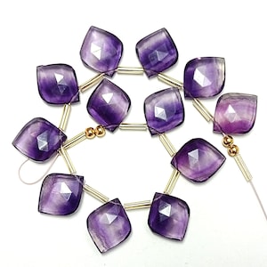 May include: A strand of purple faceted gemstone beads with gold spacers. The beads are strung on a white thread.