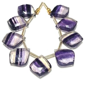 May include: A strand of purple and white fluorite gemstone beads, each bead is faceted and has a unique pattern. The beads are strung on a gold wire and are ready to be made into jewelry.