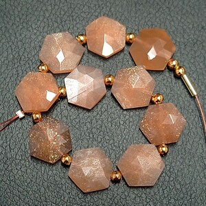 May include: A strand of 10 faceted, hexagonal sunstone beads with a copper-toned metallic sheen. The beads are strung on a copper-toned wire with small copper-toned beads between each sunstone bead.
