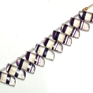 May include: A strand of ten faceted fluorite beads, each with a unique pattern of white and purple stripes. The beads are strung on silver wire with gold spacers.