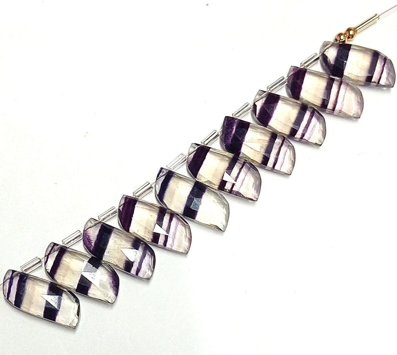 May include: A strand of ten faceted fluorite beads, each with a unique pattern of white and purple stripes. The beads are strung on silver wire with gold spacers.