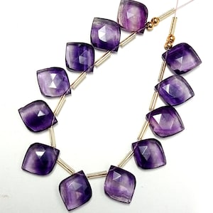 May include: A strand of purple amethyst gemstone beads with faceted, square-shaped beads. The beads are strung on gold-colored wire with small gold spacers between each bead.