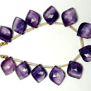May include: A strand of purple amethyst gemstone beads with a faceted, teardrop shape. The beads are strung on a gold wire with gold spacers.