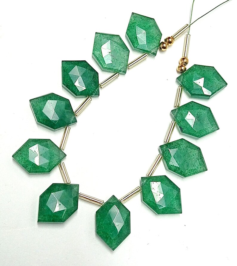 May include: A strand of green gemstone beads with faceted edges, separated by gold spacers. The beads are strung on a clear thread.