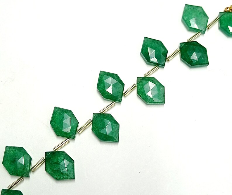 May include: A strand of green gemstone beads with faceted edges. The beads are strung on gold-colored wire.
