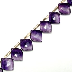 May include: A strand of faceted amethyst gemstone beads, each bead is a teardrop shape with a pointed tip and a flat base. The beads are strung on a gold wire.
