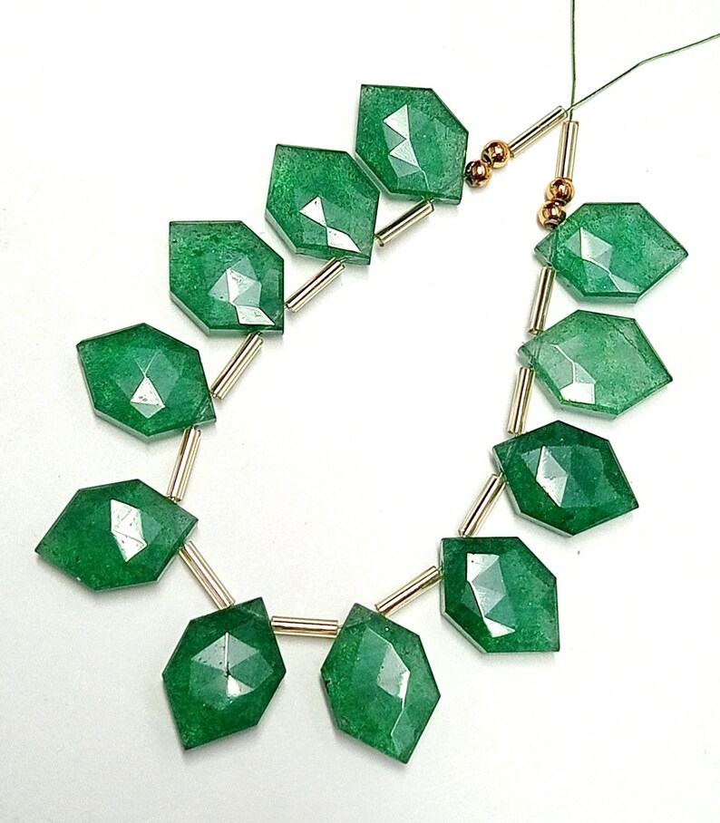 May include: A strand of green gemstone beads with gold spacers. The beads are faceted and have a slightly irregular shape.