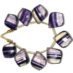 May include: A strand of purple and white fluorite gemstone beads with gold spacers. The beads are faceted and have a natural, irregular shape.