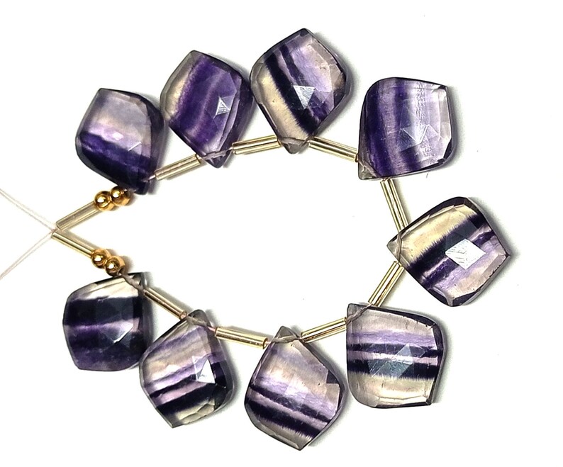 May include: A strand of purple and white fluorite gemstone beads with gold spacers. The beads are faceted and have a natural, irregular shape.