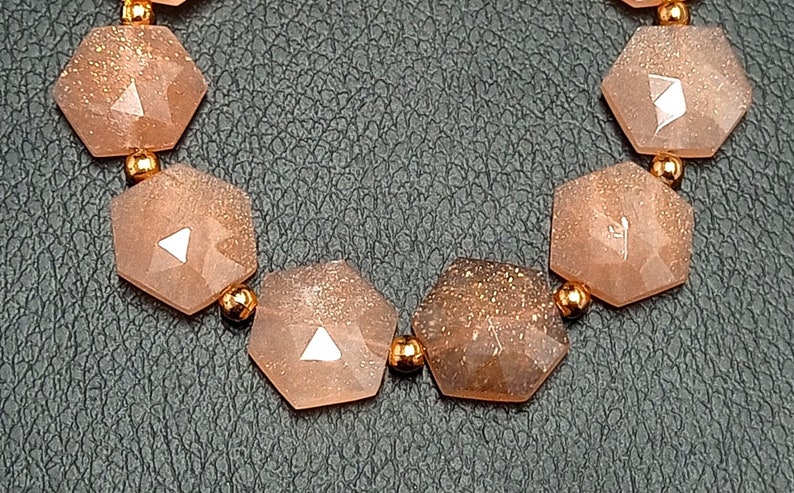 May include: A bracelet made of light brown sunstone beads with a hexagonal shape. The beads are connected with small gold-colored metal beads.