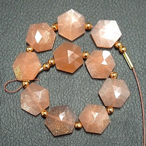 May include: A strand of faceted sunstone beads in a peachy-orange color with gold flecks. The beads are strung on a wire with gold-toned spacers.