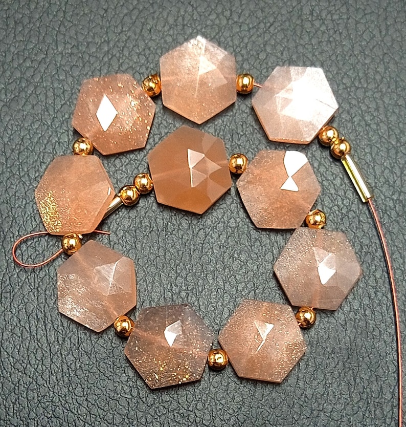 May include: A strand of faceted sunstone beads in a peachy-orange color with gold flecks. The beads are strung on a wire with gold-toned spacers.