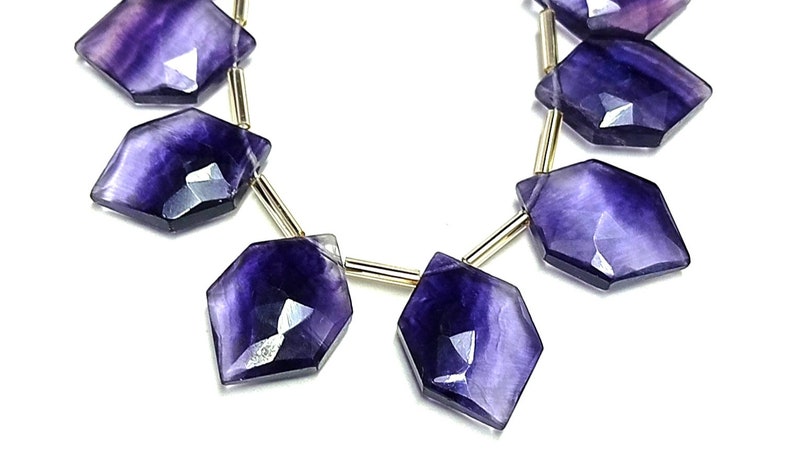 Puede incluir: Hilo de cuentas facetadas de fluorita p&uacute;rpura. Cada cuenta tiene una forma geom&eacute;trica &uacute;nica con una superficie pulida y reflectante. Las cuentas est&aacute;n ensartadas en un alambre dorado, creando un hermoso contraste. Ideal para la fabricaci&oacute;n de joyas.