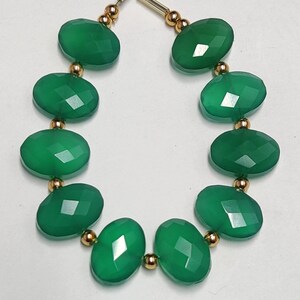 Puede incluir: Una hebra de cuentas de piedras preciosas verdes con separadores dorados. Las cuentas son de forma ovalada y tienen un acabado facetado.