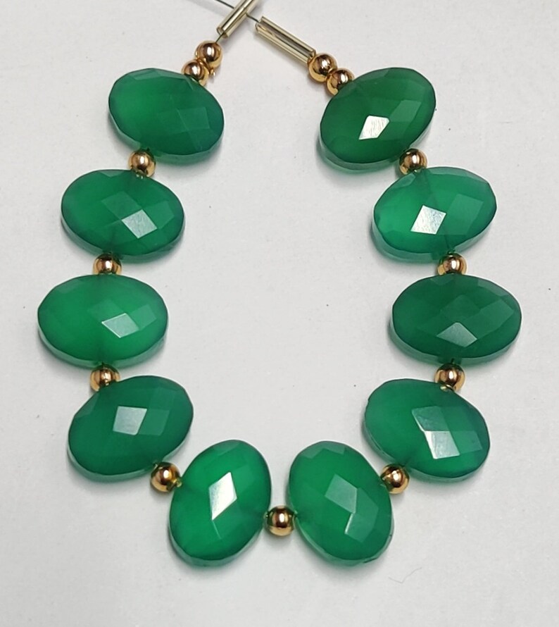 Puede incluir: Una hebra de cuentas de piedras preciosas verdes con separadores dorados. Las cuentas son de forma ovalada y tienen un acabado facetado.